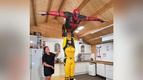 Baker Lara Mason smiled and points to her cake sculpture of Marvel superheros Deadpool and Wolverine, with Wolverine lifting Deadpool in the air in a recreation of the Dirty Dancing lift