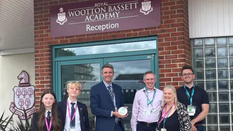 Staff and two pupils standing outside academy entrance with award plaque