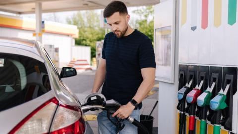 Young man wearing a blue striped T-shirt filling a car with petrol