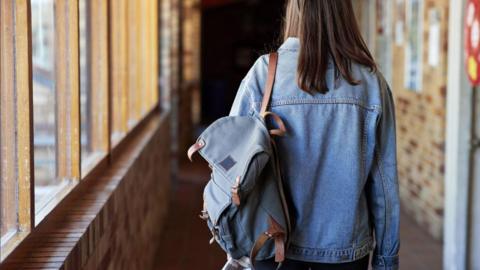 Rear view of young woman with backpack (rucksack or satchel drapped over shoulder) walking in corridor