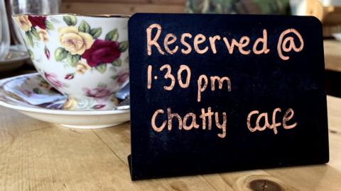 A cup and saucer and a sign reserving the table for Chatty Cafe