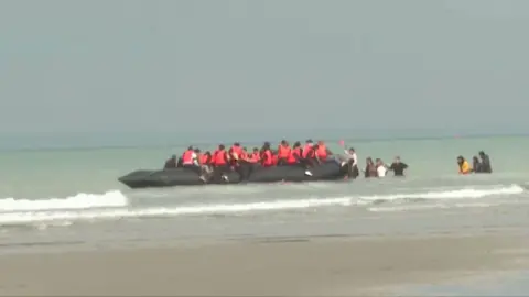 A group of migrants, a number of whom are wearing life jackets, can be seen crowded into the boat.