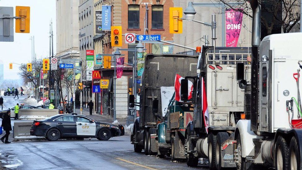 A line of trucks parks on a road in downtown Ottawa with police nearby during anti-vaccine mandate protests earlier this year.