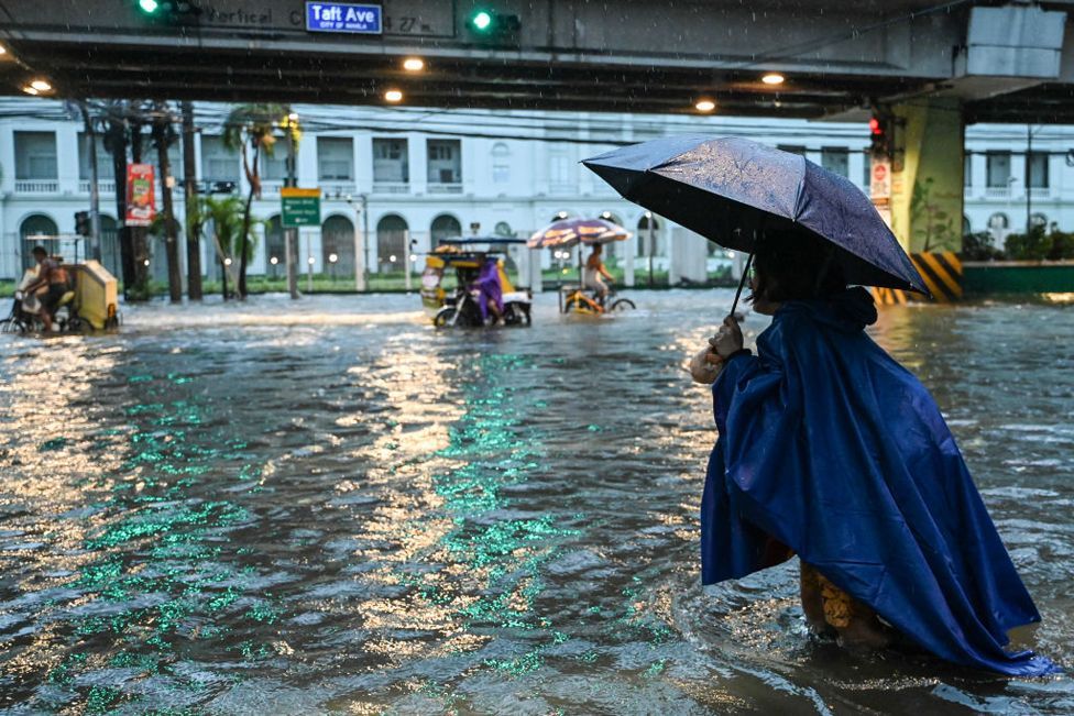 People walk along a flooded street in Manila on July 24, 2024 amid heavy rains brought by Typhoon Gaemi. 