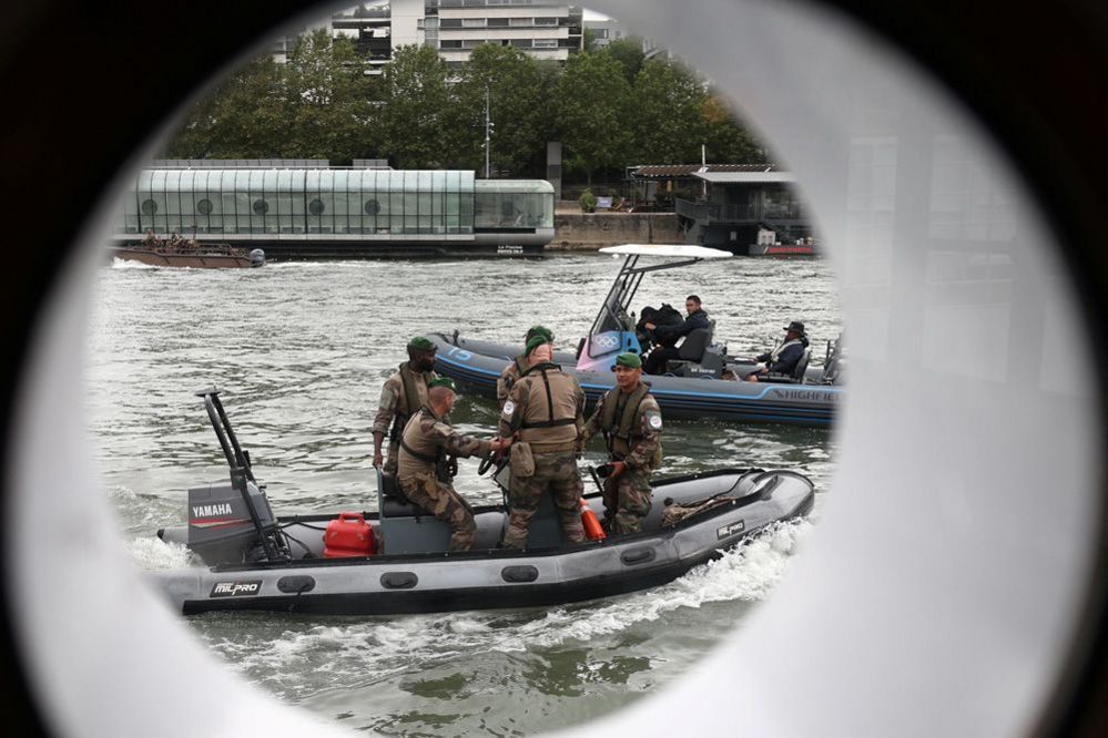 Members of the French Armed Forces in a motor boat are seen through a boat's porthole on the river Seine as they patrol prior to the opening ceremony of the Paris 2024 Olympic Games in Paris