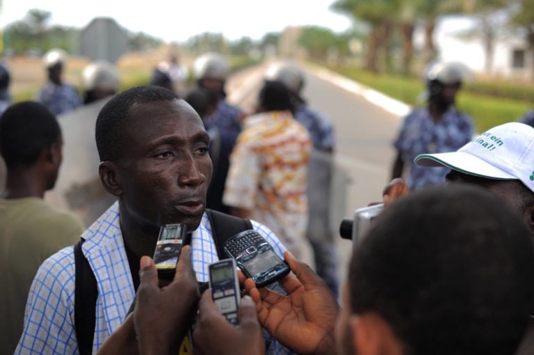 El periodista Ferdinand Ayité habla con la prensa, mientras que la policía trata de suprimir una protesta en frente del Palais des Congrès, Lomé, Togo, el 19 de febrero de 2013, Daniel Hayduk/AFP via Getty Images