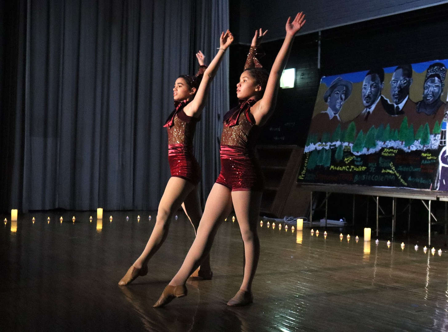 Two dancers on stage with flameless candles with their airs up and bent back