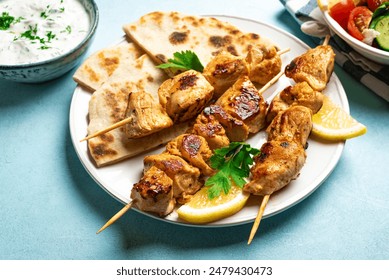 Chicken souvlaki kebabs, herbed yogurt sauce and pita flatbread close up. Mediterranean healthy meal - homemade meat skewers and oraganic green salad with yogurt sauce, balanced keto food.