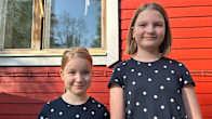 Kaksi alakoululaista tyttöä poseeraa punaisen lautaseinän vieressä.