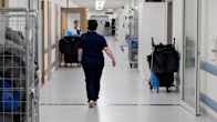 Photo shows a healthcare worker walking down a corridor in a hospital.