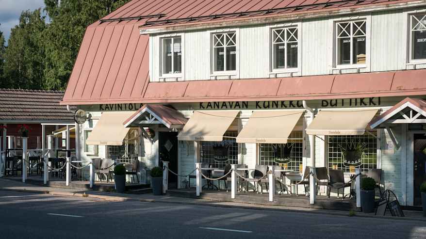 Gammalt vitt trähus med rött plåttak som inrymmer restaurang med uteservering.