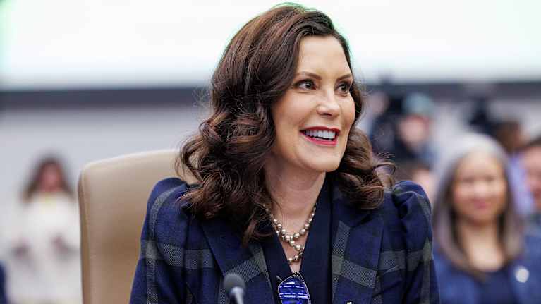 Gretchen Whitmer hymyilee. Edustalla mikrofoni, tausta epäselvä.