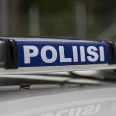 Närbild på polisskylt med blåljusen på i en polisbil. 