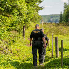 Two Border Guard officers wearing black uniforms, walking along the Finnish-Russian border.