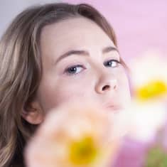 Malin Öhman står med några vita och gula anemoner framför ansiktet.