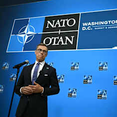 President Alexander Stubb framför blå bakgrund med Natotoppmötets logo. 