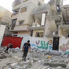 Två barn går bland spillror framför en betongbyggnad som är sönderbombad.