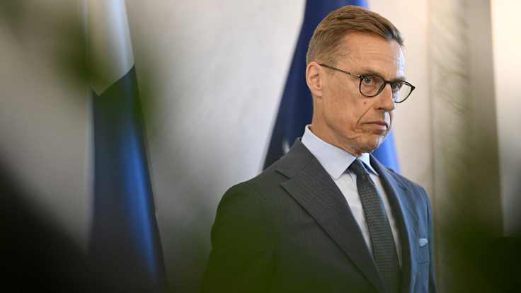 Stubb stands in front of the Finnish flag looking serious.