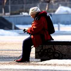 En äldre kvinna och en yngre person sitter med ryggarna mot varandra vid en staty. 