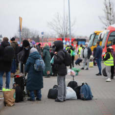 Människor står på en trottoar med resväskor, ryggsäckar och andra väskor.
