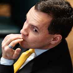 Close-up photo of Wille Rydman, wearing a dark suit and yellow necktie.