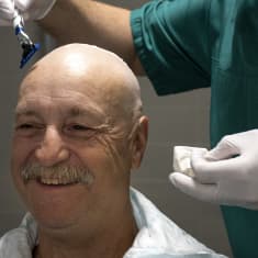En person rakar huvudet på en man som ler.