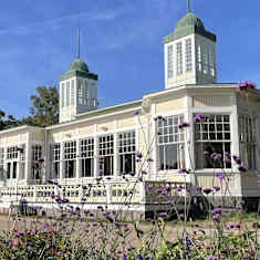 Hangö Casino i höstsol. En gammal vit byggnad med många sirliga fönster. I förgrunden lila blommor.