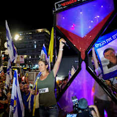 Mielenosoittaja pitää mikrofonia ojennetussa kädessään lippujen ja banderollien keskellä.