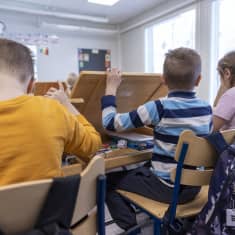 Barn som gräver fram saker ur sina pulpeter i skolan. 