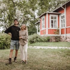 Två personer står bredvid varandra på en gräsmatta och ler. I bakgrunden syns ett rött hus.