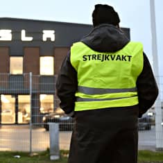 En strejkvakt i gul väst står utanför stängslet kring Teslas logistikcentral.