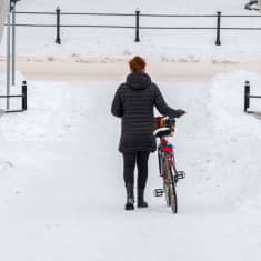 En kvinna leder en cykel ner för en bro.