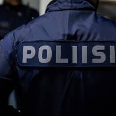 På bilden syns en person i polisdräkt. Personen står med ryggen till med texten "poliisi" på ryggen.