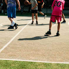 Ryhmä koululaisia pelaa koripalloa aurinkoisella kentällä.