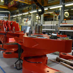 En stor röd del av en lastare ligger på golvet i en fabrik.
