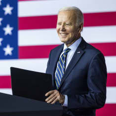 Joe Biden seisoo puhujanpöntössä taustallaan Yhdysvaltain lippu.