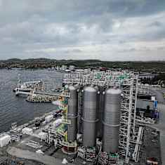 Aerial view of an industrial facility on the seaside with large metal cylindrical storage units.