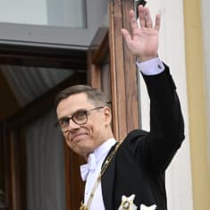 Alexander Stubb i festkläder vinkar från en balkong och ler.