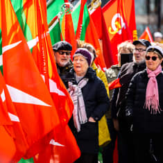 Förstamajtåg i Helsingfors i solsken, med röda flaggor och åldrande deltagare