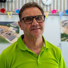 En leende medelålders man i glasögon och grön kragskjorta. På väggen bakom honom syns bilder på industriella anläggningar.