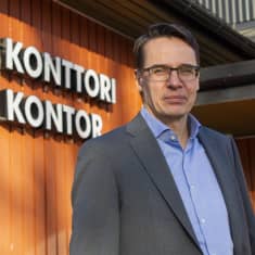 Måns Holmberg står utomhus, bakom honom syns en fasad där det står kontor på finska och svenska.