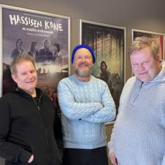 Muusikot Hannu Porkka ja Jussi Kinnunen sekä dokumentti- ja TV-ohjaaja Antti Kuivalainen poseeraavat Hassisen Kone dokumentin julisteen äärellä.