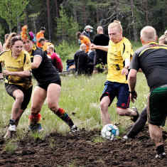Naisia ja miehiä pelaamassa suopotkupalloa soisella kentällä.