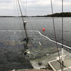 En stor båt med mast, kanske trålare som håller på att sjunka i vatten, nära strand.