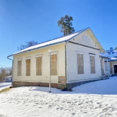 En ljus större träbyggnad med vanerskivor på fönstren. Snö, solsken.