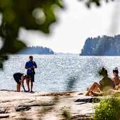 Människor som sitter eller står och solar sig på en klippa invid havet. 