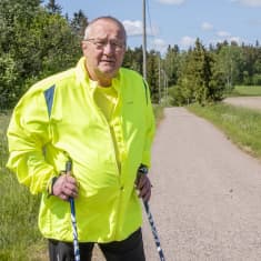 En man i reflexgul jacka står med sina vandringsstavar på en gång- och cykelväg. Han tittar in i kameran.