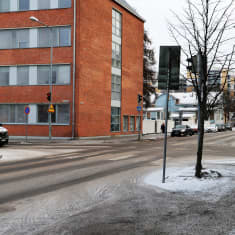 En gata med lite snö på och ett tegelfärgat hus. 