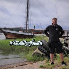 En medelålders man står i en strand framför en träskuta.