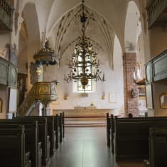 Kyrkbänkar, prediksstol och altare i en medeltida stenkyrka.